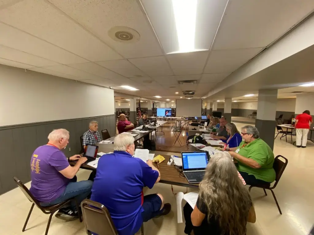 Council members seated around tables with laptops and papers during a meeting