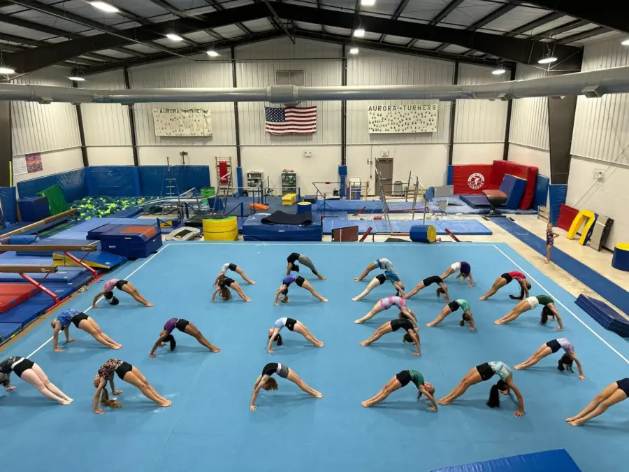Rows of young gymnasts holding backbends on the floor mat during Aurora Turners practice