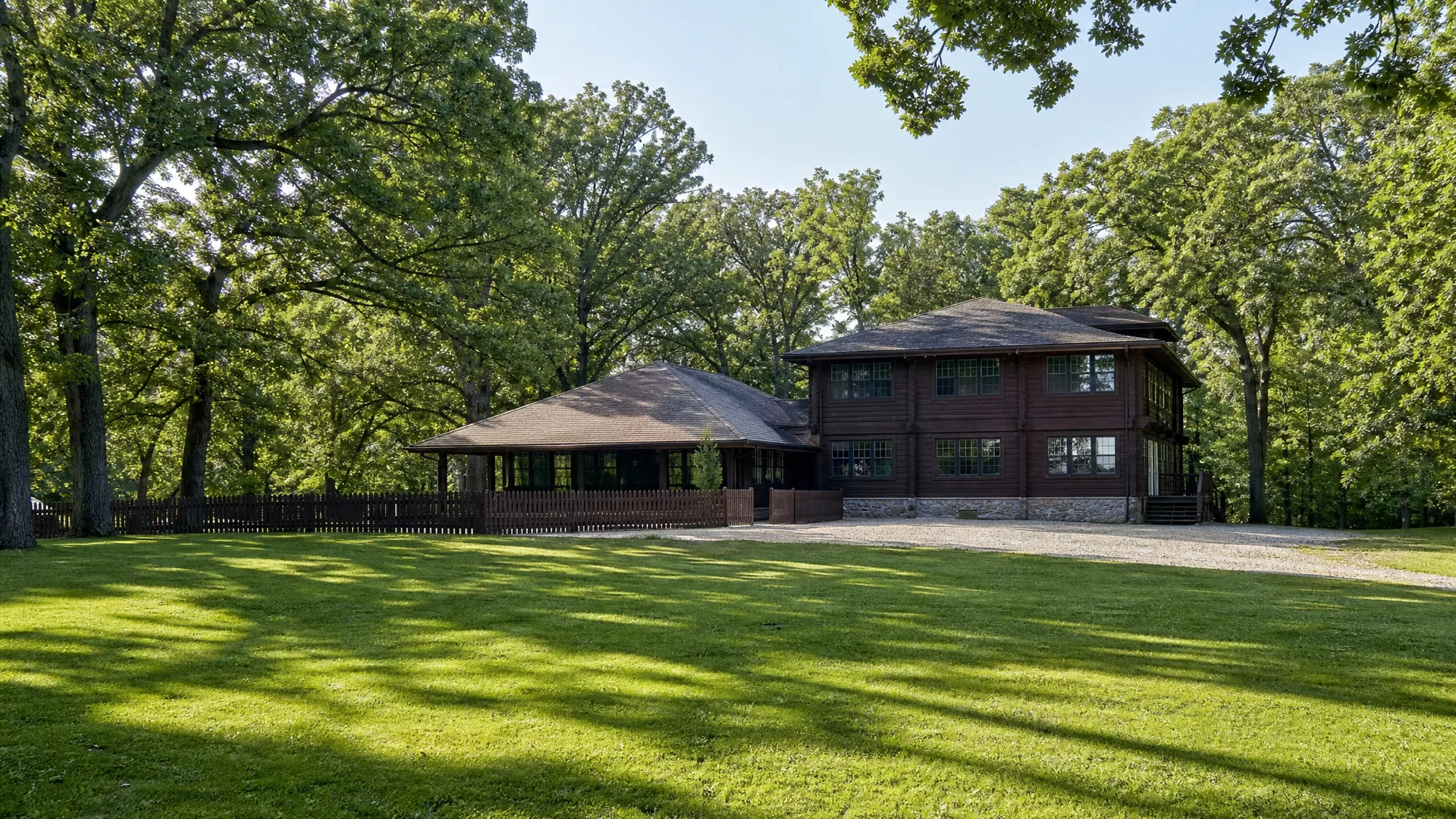 The two-storey brown timber clubhouse and its pavilion seen across the mown commons at Illinois Turners Camp on a summer morning